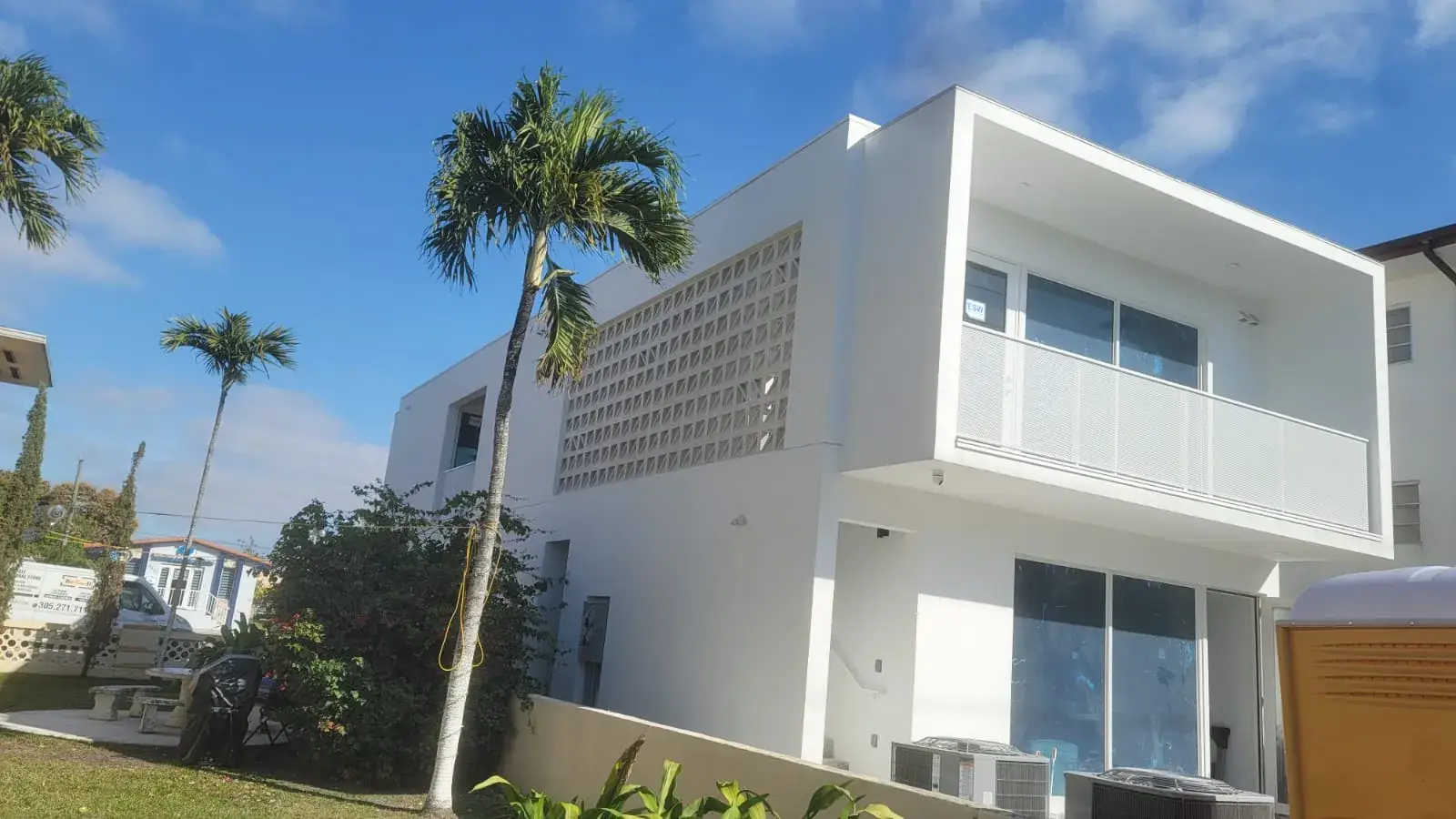 White condominium exterior with breeze-block screen wall, perforated-metal balcony rails, and palms