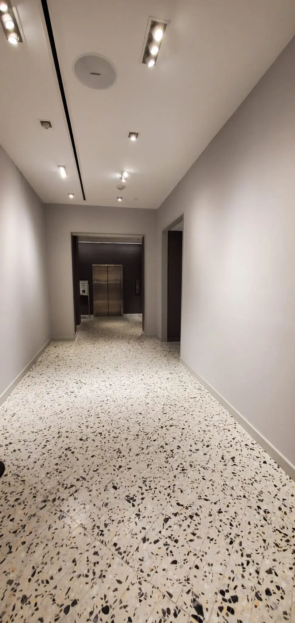 Service corridor to the elevator lobby with terrazzo floor and track lighting
