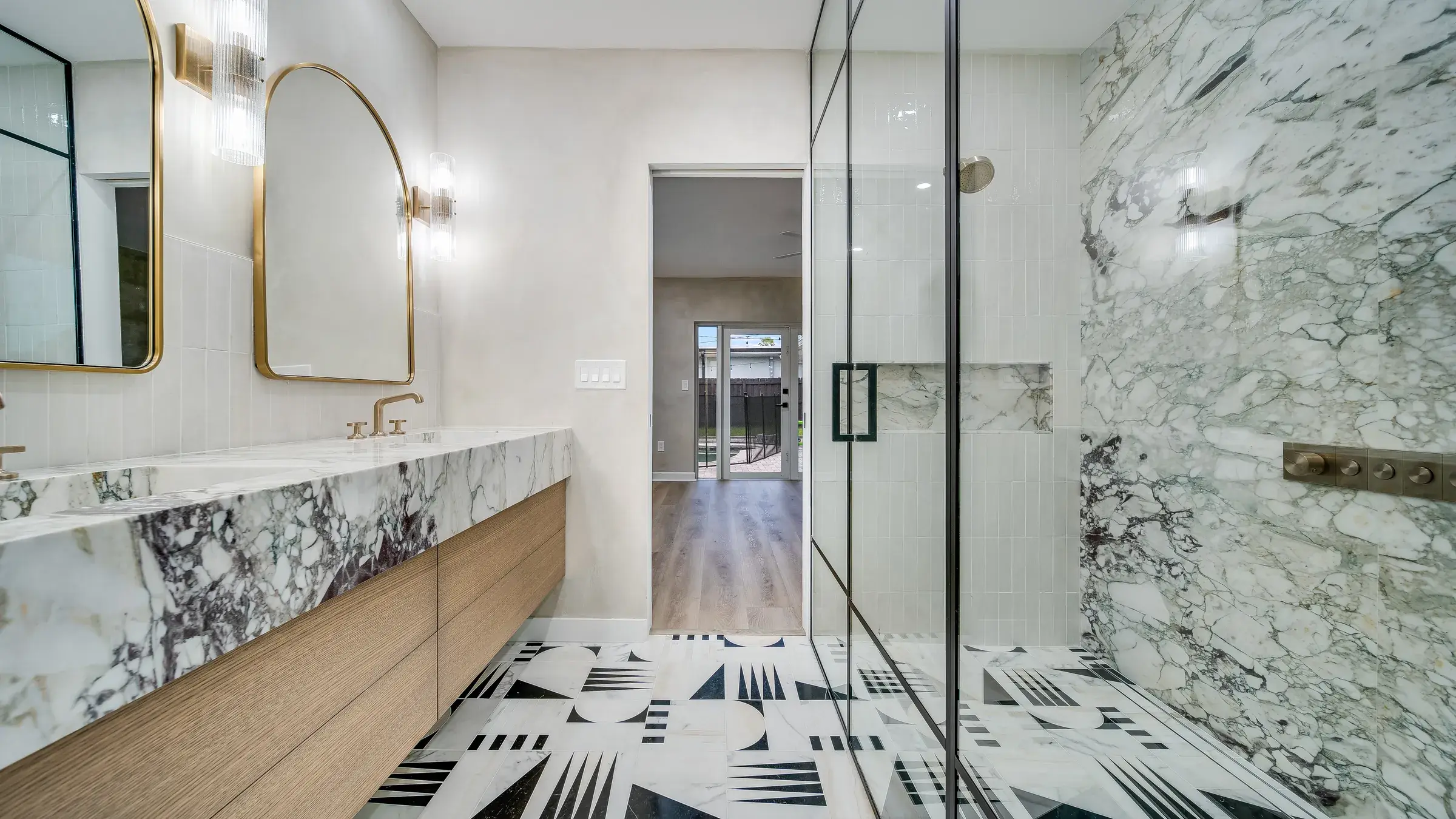 Vanity on the left, marble shower on the right, with the sightline through the bedroom to the pool doors