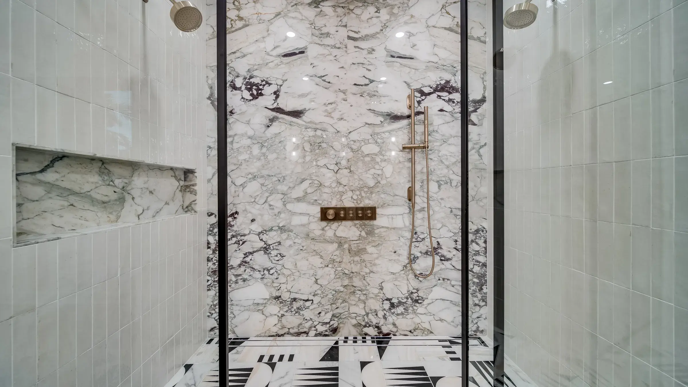 Shower interior, centered on the marble feature wall with brass control panel, hand shower, dual heads and tile niche