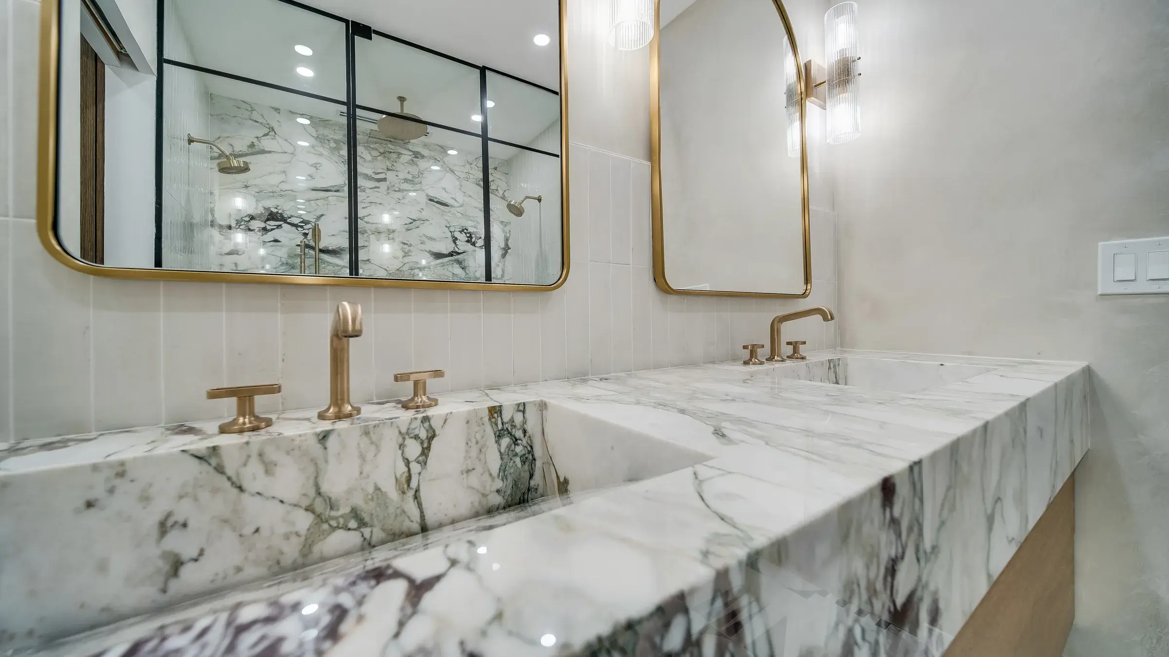Thick marble slab edge of the vanity with brass widespread faucets and the shower in the mirror