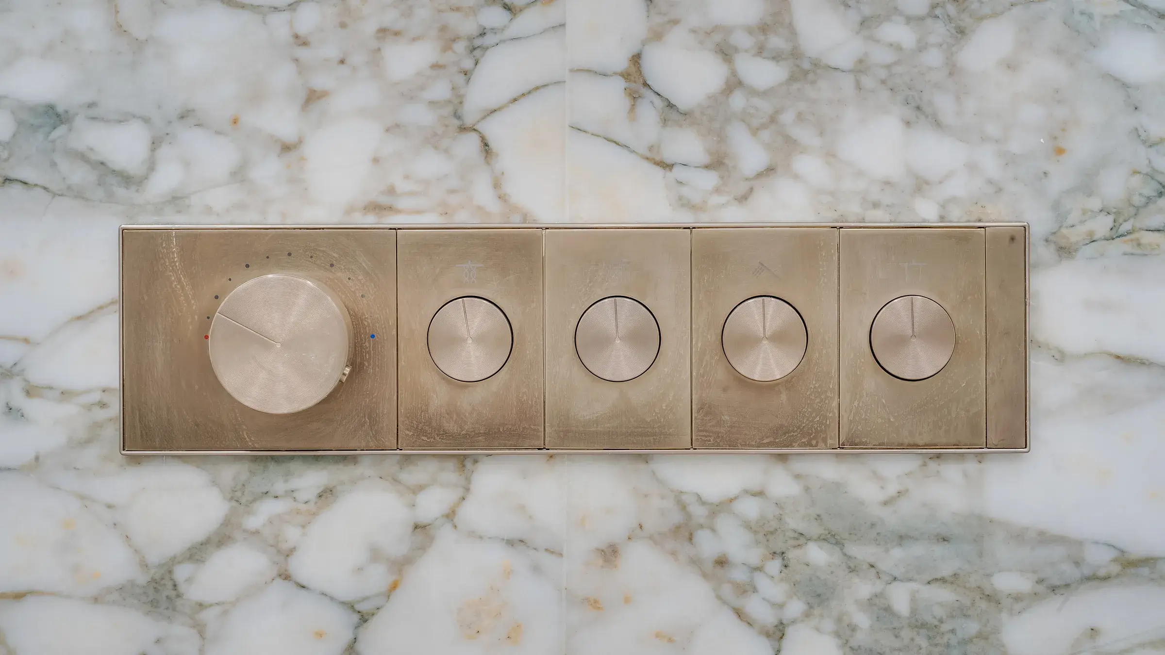 Brushed-brass thermostatic control panel set flush into the marble