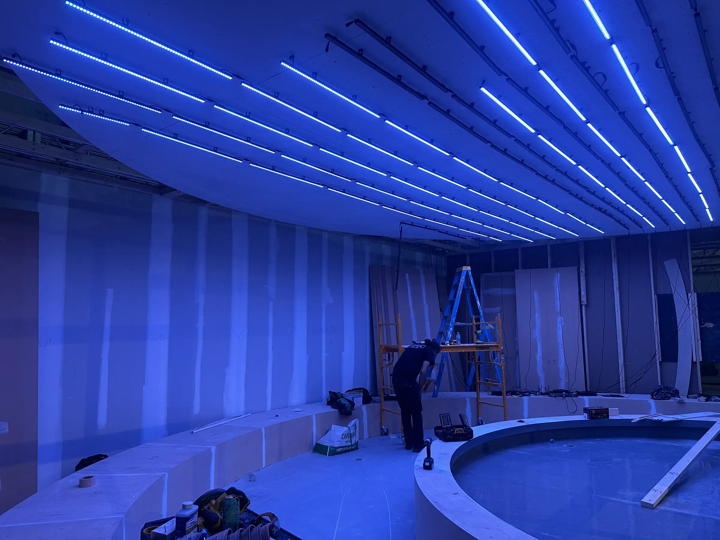 Blue LED strips across the curved ceiling during install, with the basin in the foreground