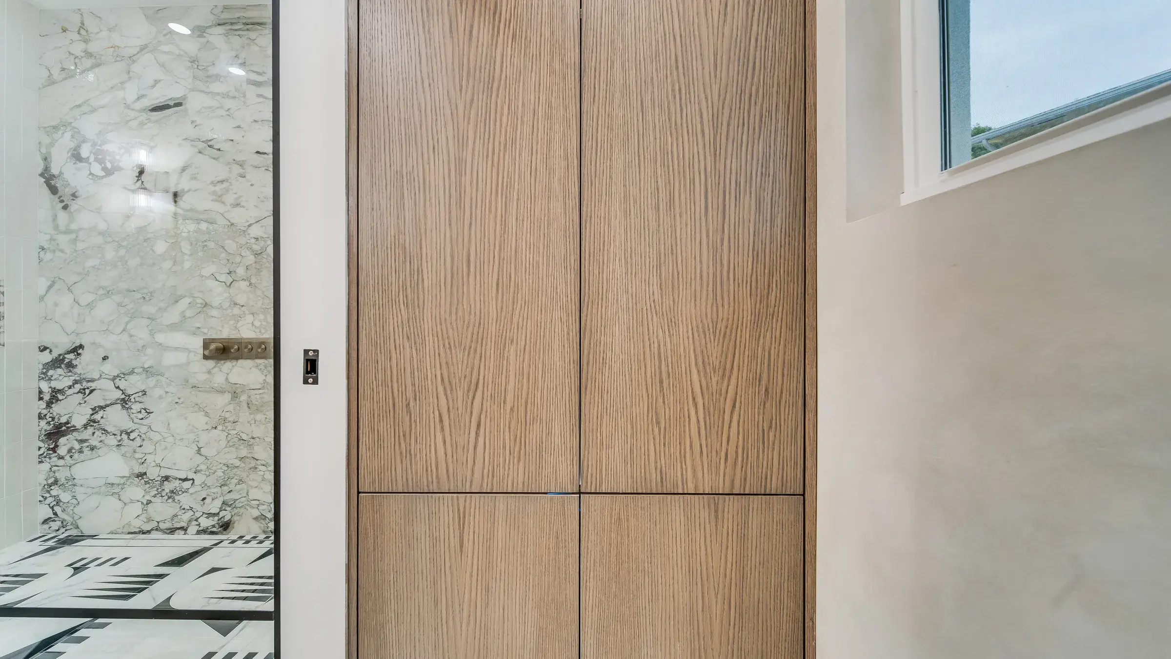 Tall oak linen cabinet beside the marble shower
