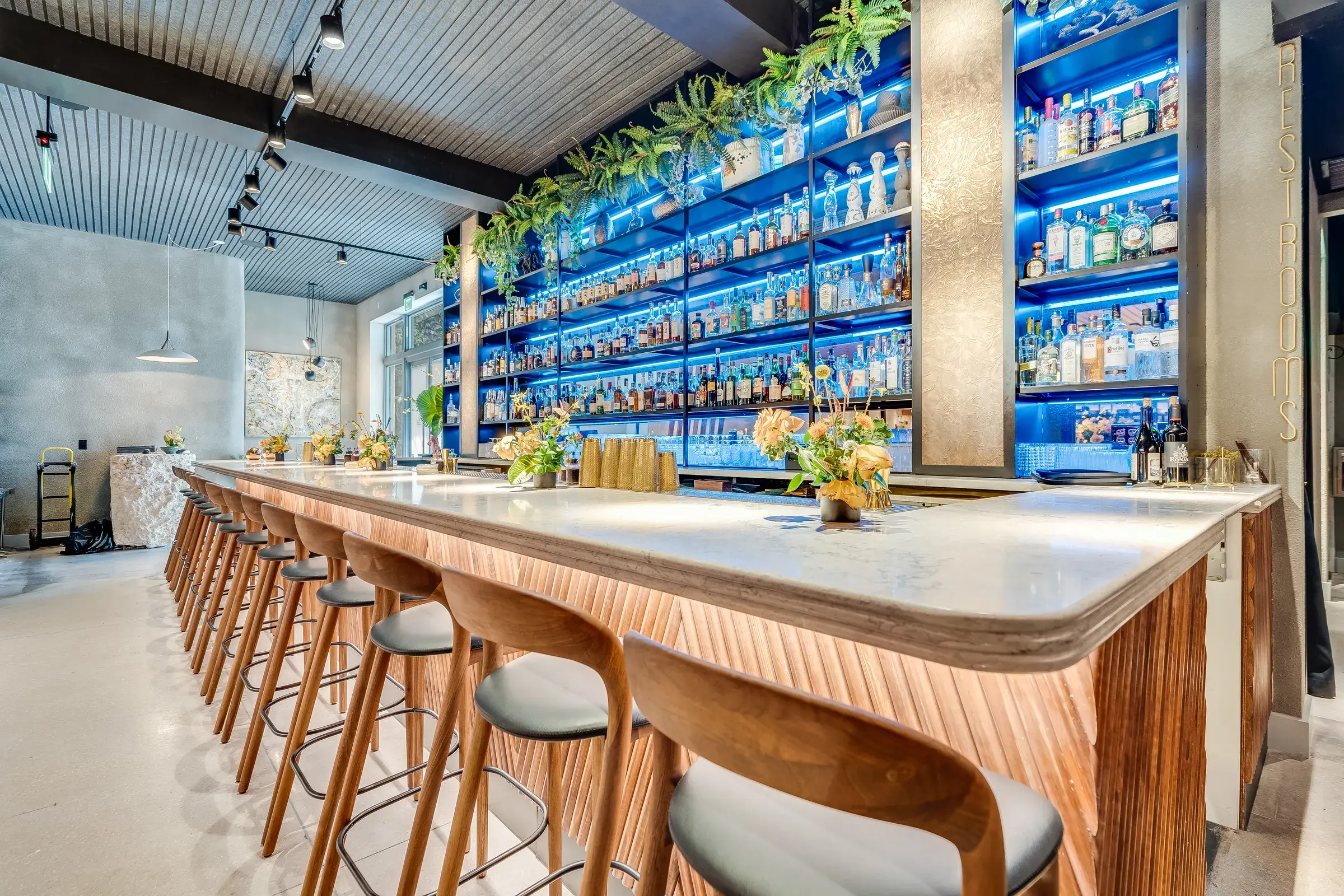 One-point view down the marble bar with the chevron tambour face and glowing back bar