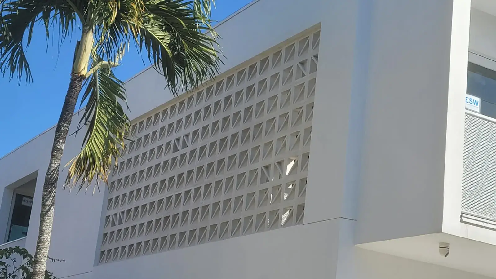 White low-rise with decorative breeze-block screen wall, royal palm and clear blue sky